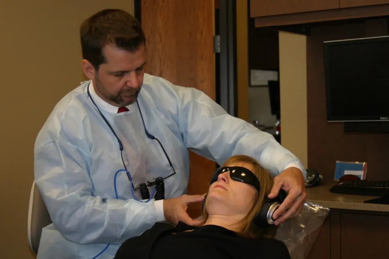 A dentist treating a reclining patient who wears an eye mask and headphones