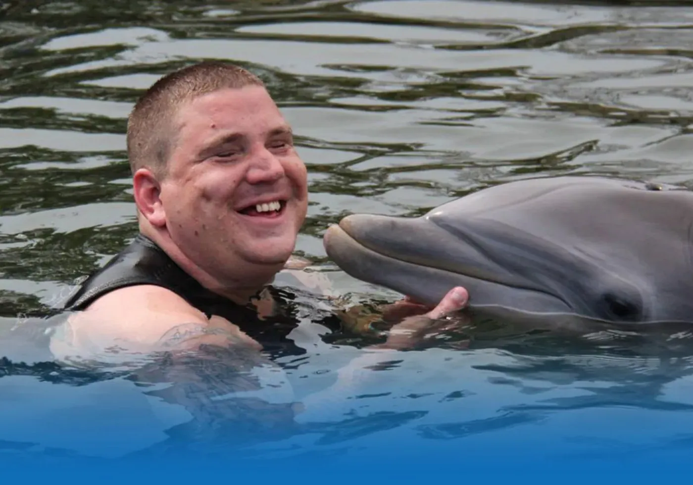 Blake smiling beside a dolphin in the water