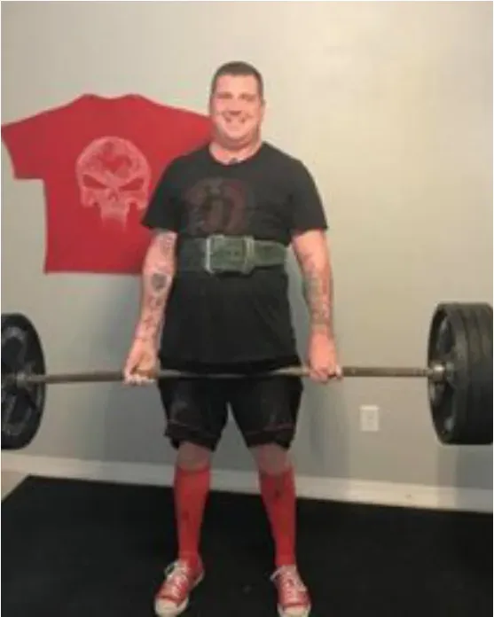Blake standing behind a loaded barbell in a gym