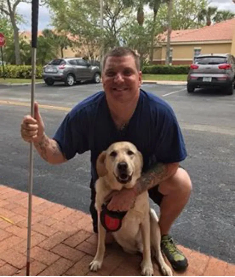 Blake kneeling beside his service dog