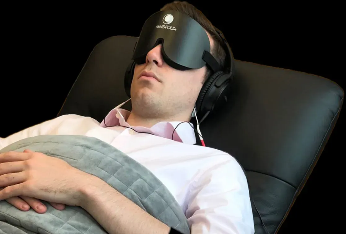 A man in a dress shirt reclining under a blanket with a NuCalm eye mask and headphones