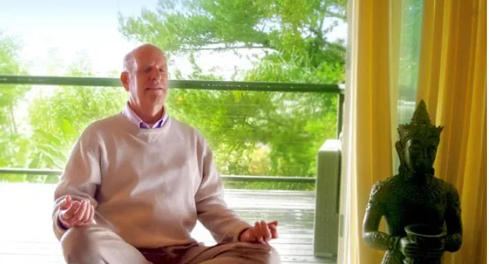 A man meditating cross-legged beside a Buddha statue