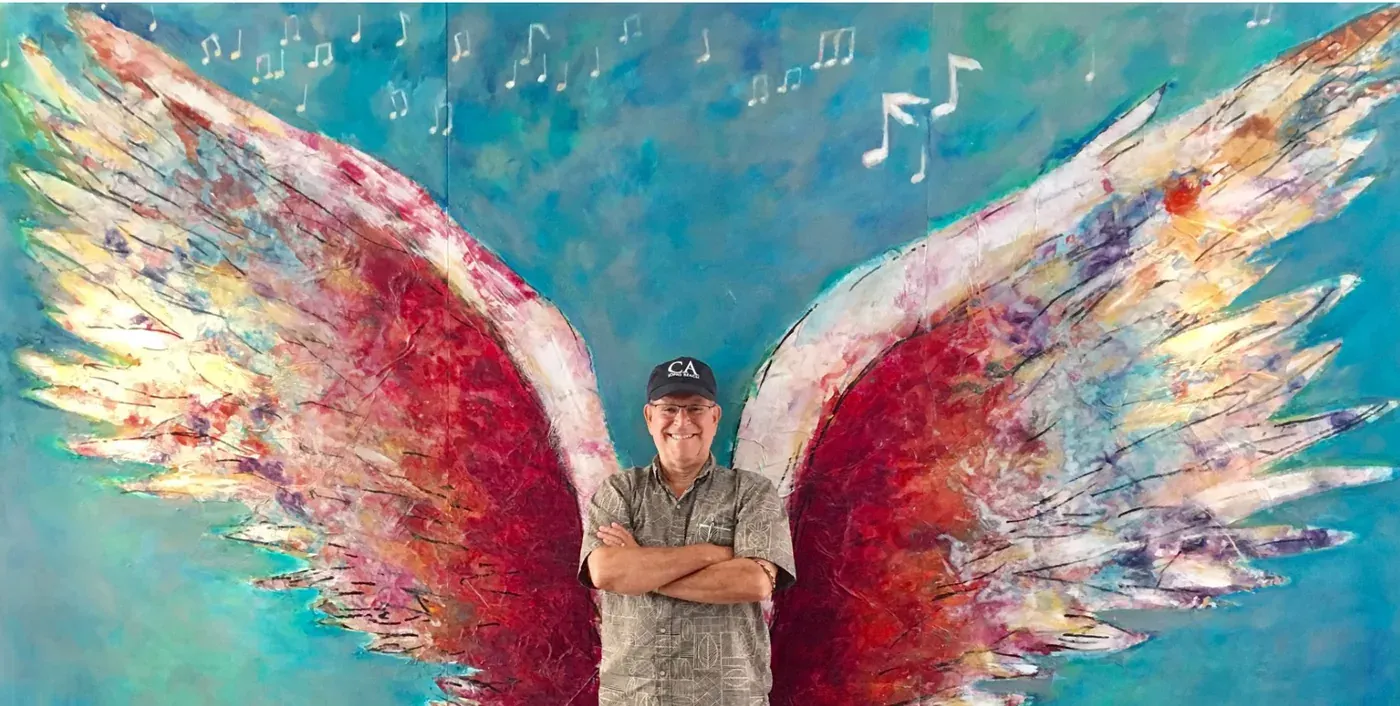 A man standing in front of a mural of painted wings
