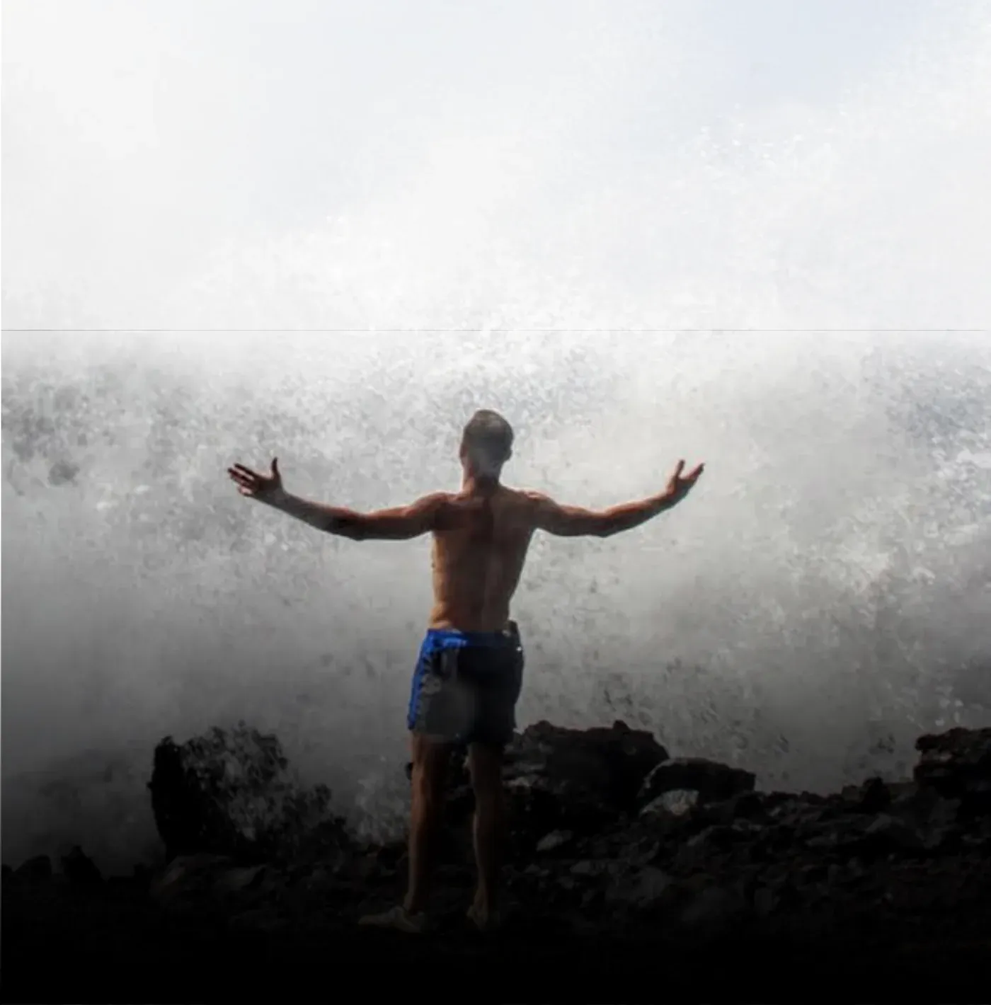Ken standing on rocks with his arms outstretched in the mist