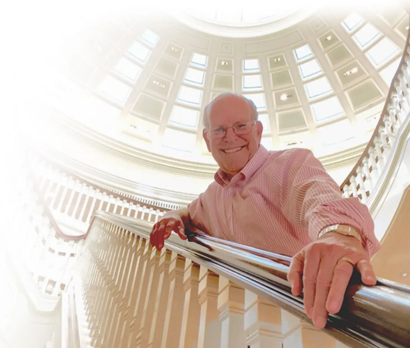 An older man leaning on a railing beneath a domed skylight