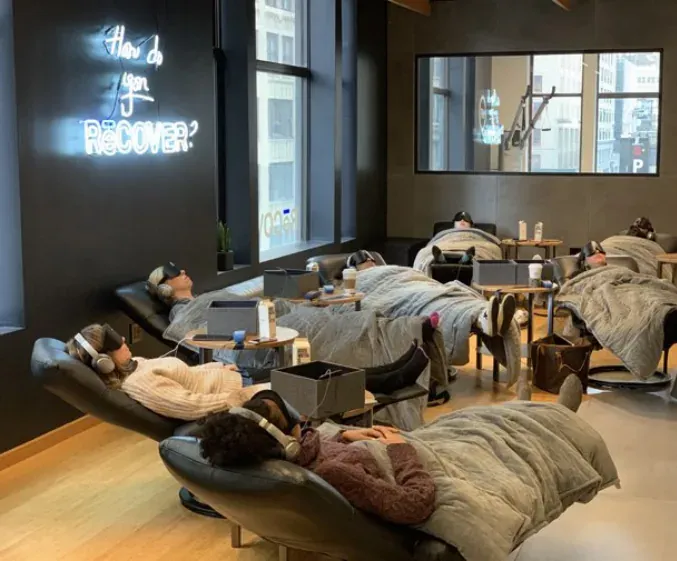 Clients reclining in the RēCOVER lounge under a neon sign