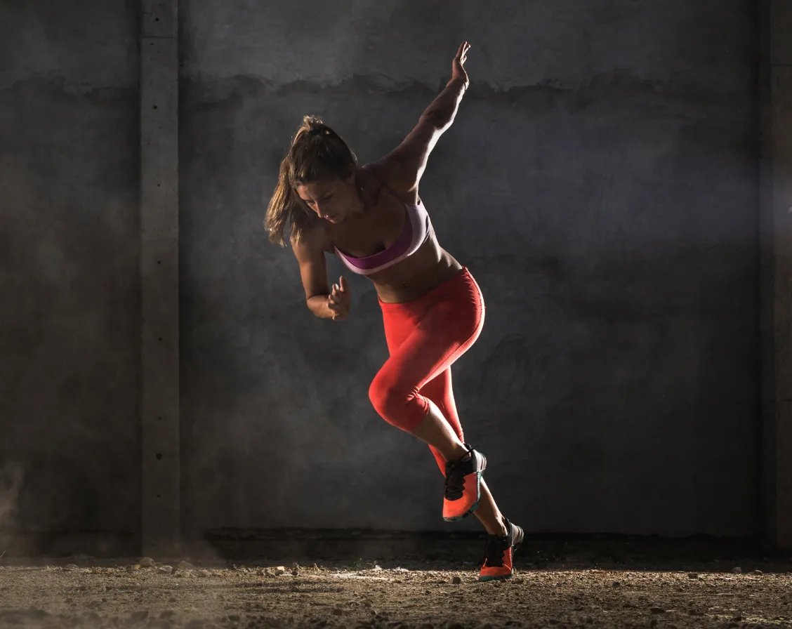 A woman in action pose, mid-run. She wears a red tank top and shorts, with red shoes.