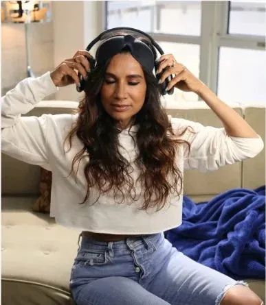 Woman putting on headphones and an eye mask on a sofa