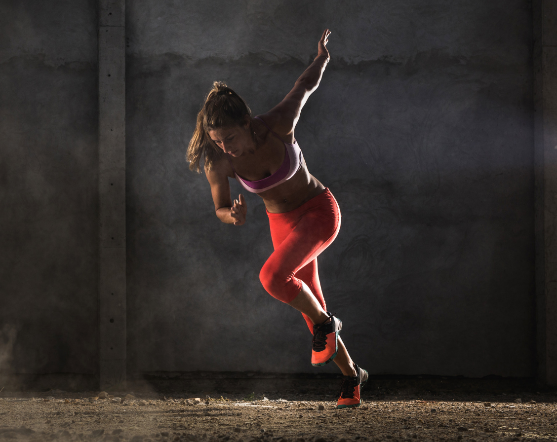 A woman in action pose, mid-run. She wears a red tank top and shorts, with red shoes.